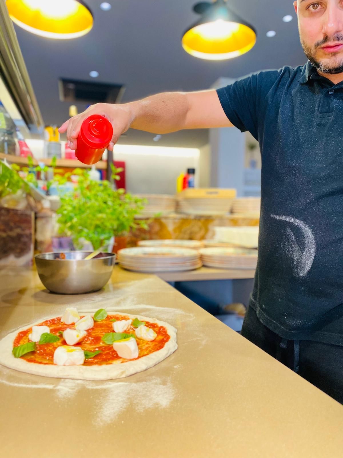 Un uomo sta versando la salsa su una pizza su un bancone