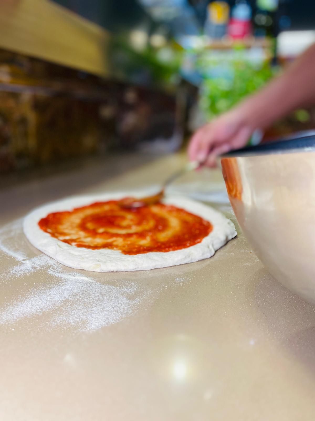 Una persona sta spalmando la salsa su una pizza su un bancone.