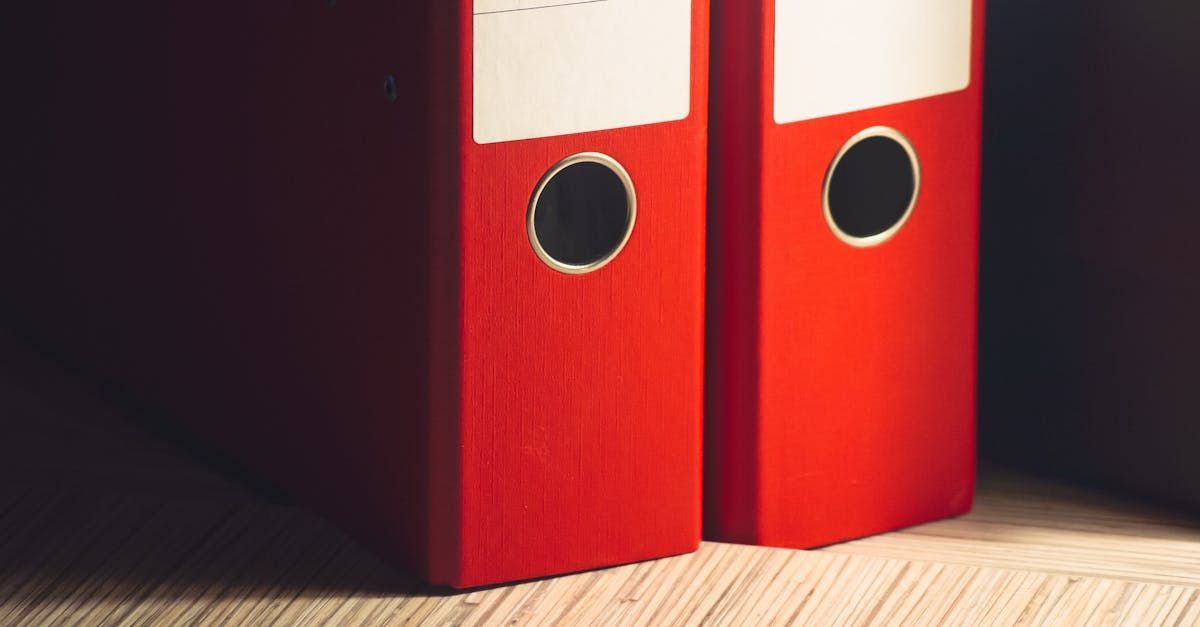 Two red binders are sitting next to each other on a wooden floor.