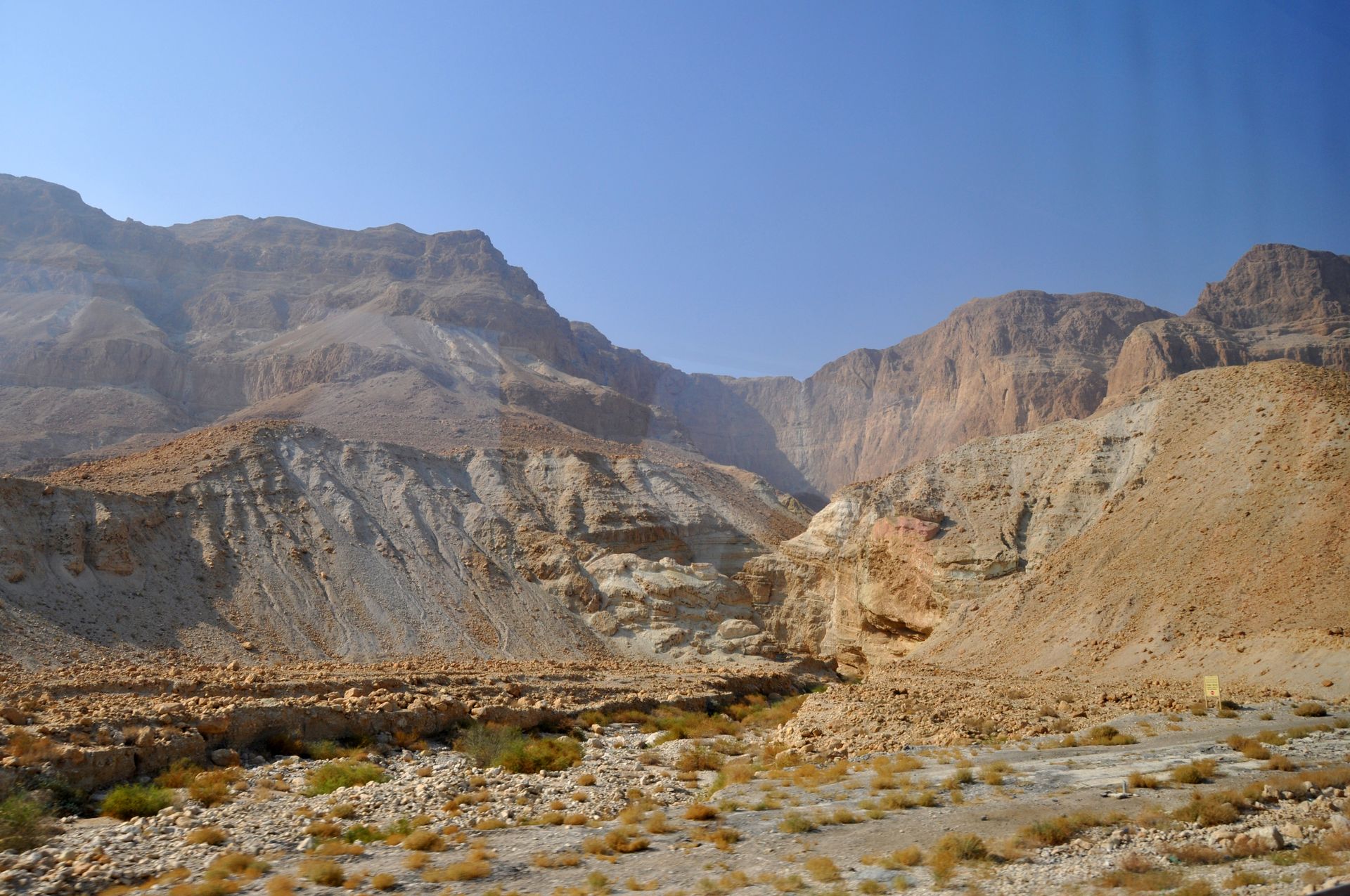 Dry, rocky canyon under a clear blue sky. Beige and brown mountains.