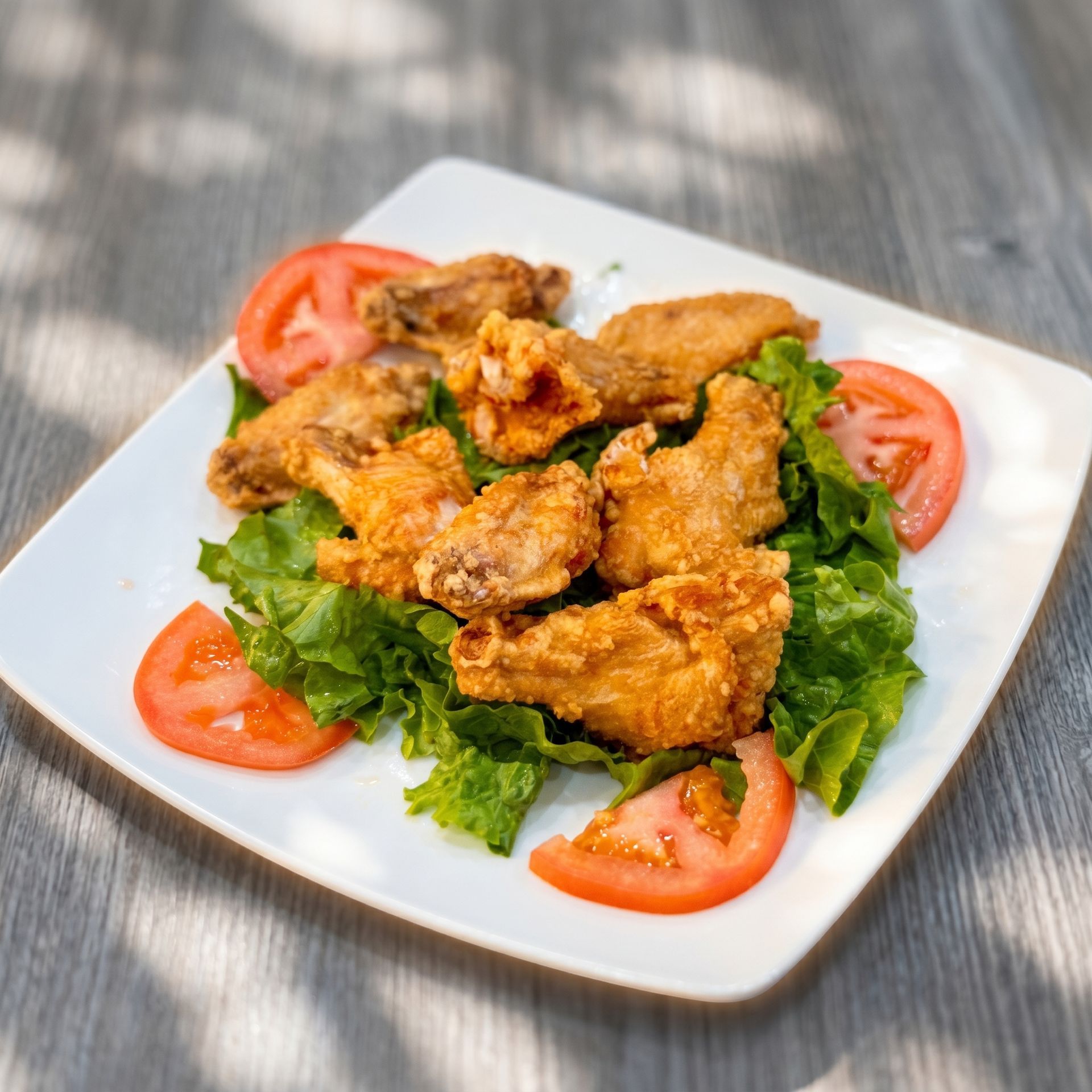 Fried chicken pieces on a white plate with lettuce and tomato slices