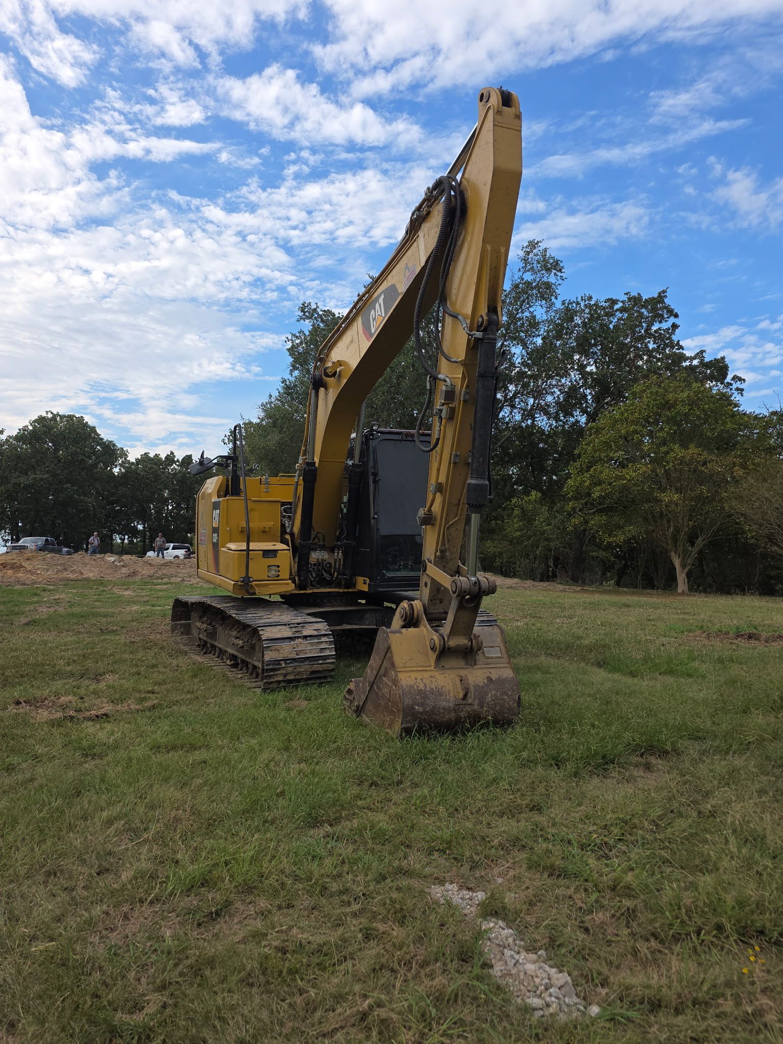 Yellow excavator in a grassy field with a blue and cloudy sky.