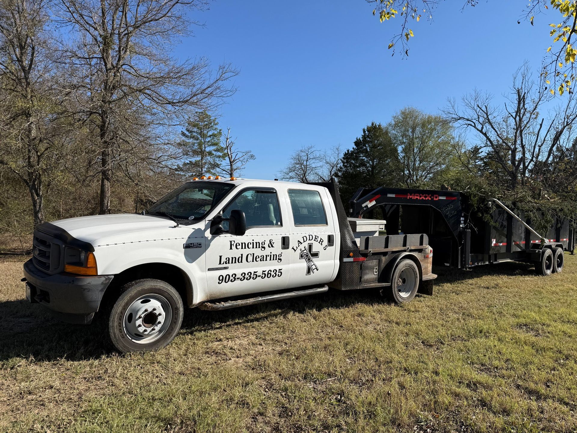 White work truck with trailer in a grassy field. Truck has company logo. Bright, sunny day.