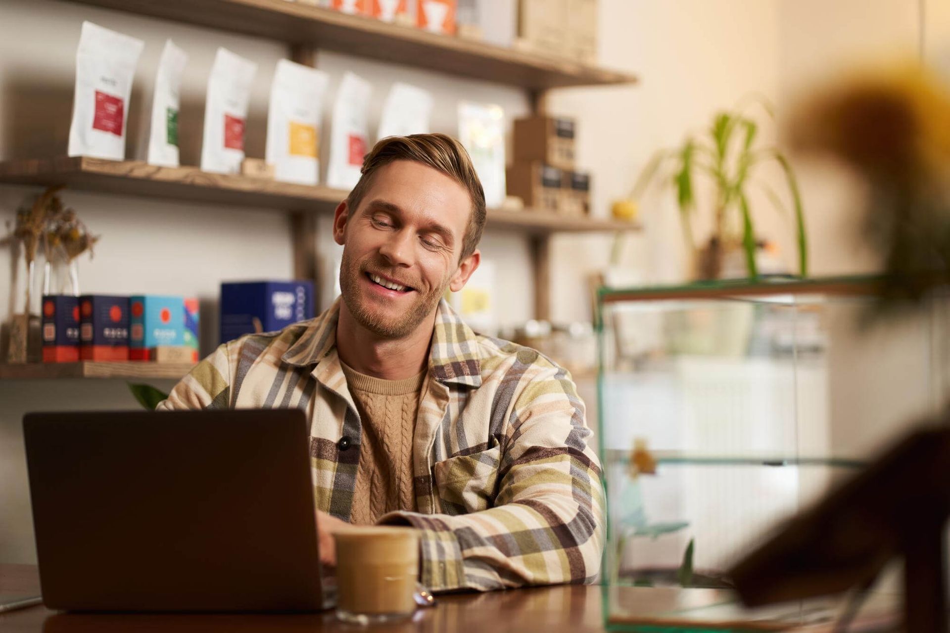 Dueño de cafetería, sonriendo, trabajando con una laptop.
