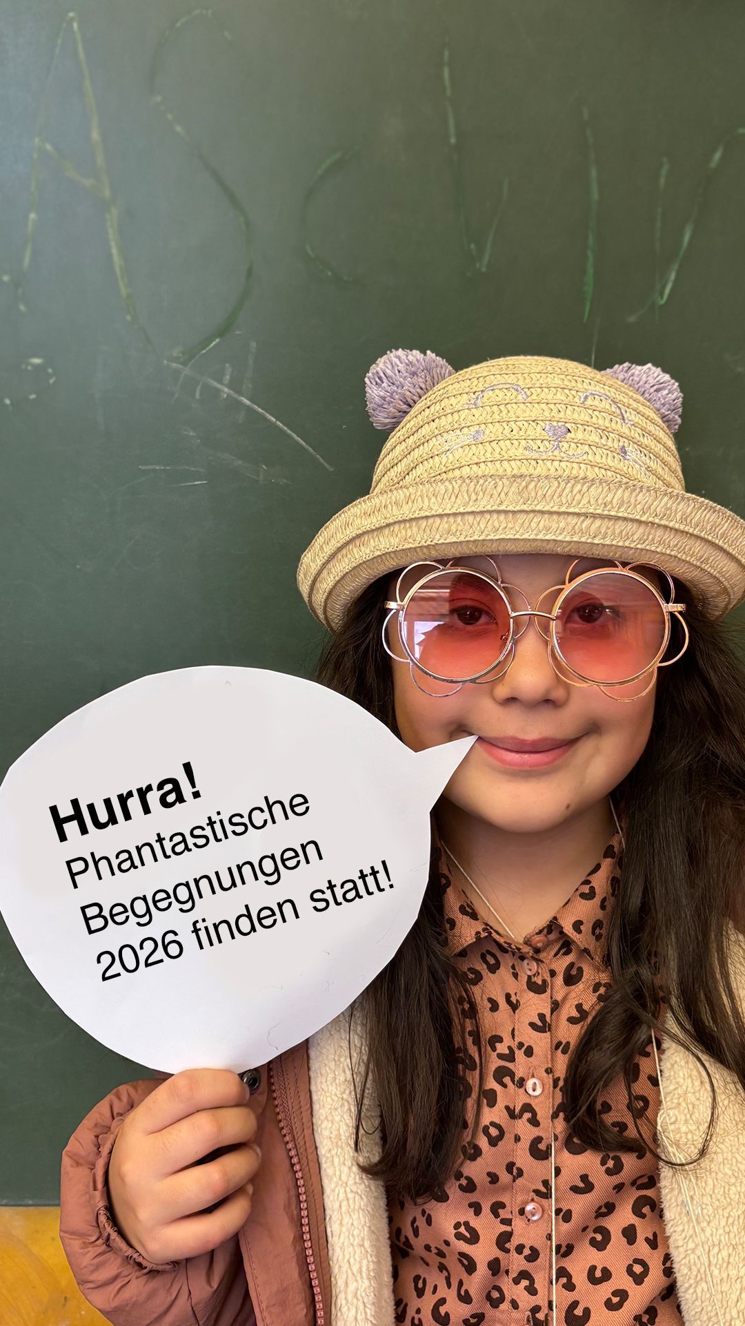 Ein Junge im Löwenkostüm bedient eine Kamera; andere Kinder tragen Hüte und stehen draußen.