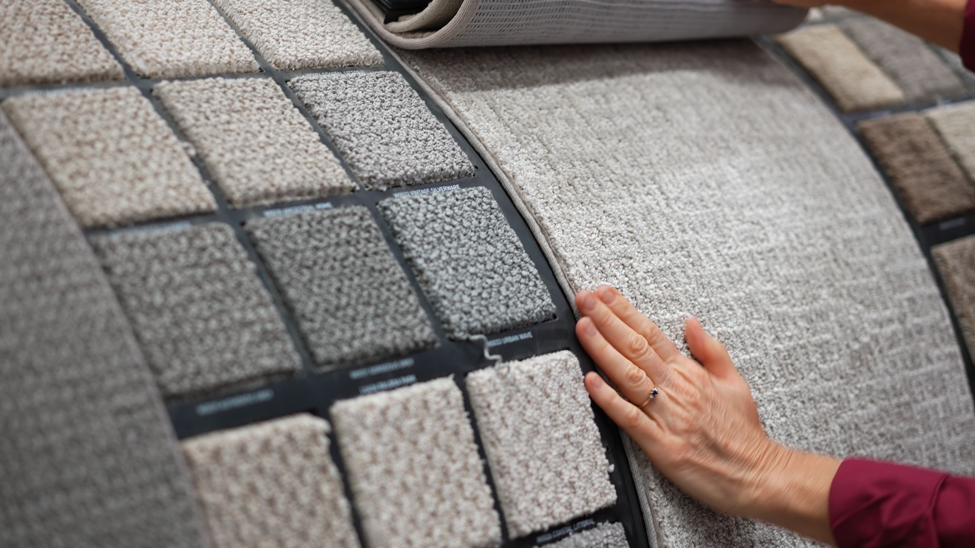 Hand selecting carpet samples from a display board with various textures and colors.