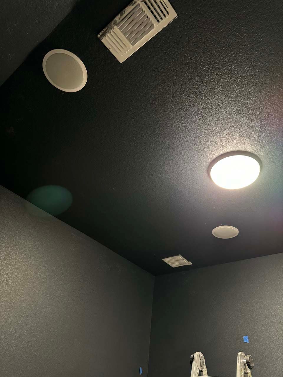 A bathroom with a black ceiling , speakers , and a light.