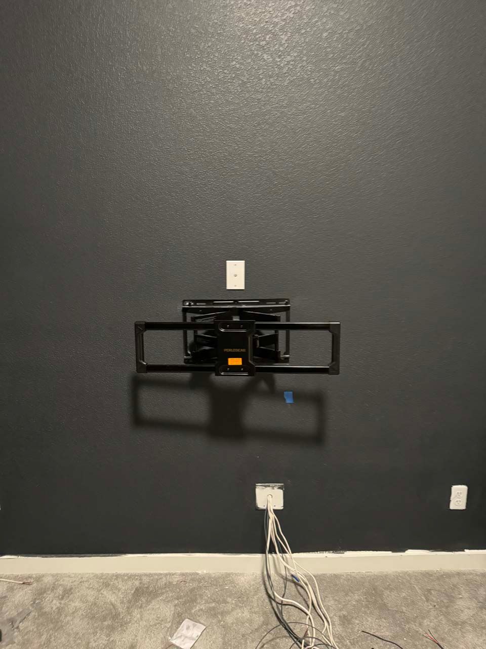A tv mount is hanging on a black wall in a room.