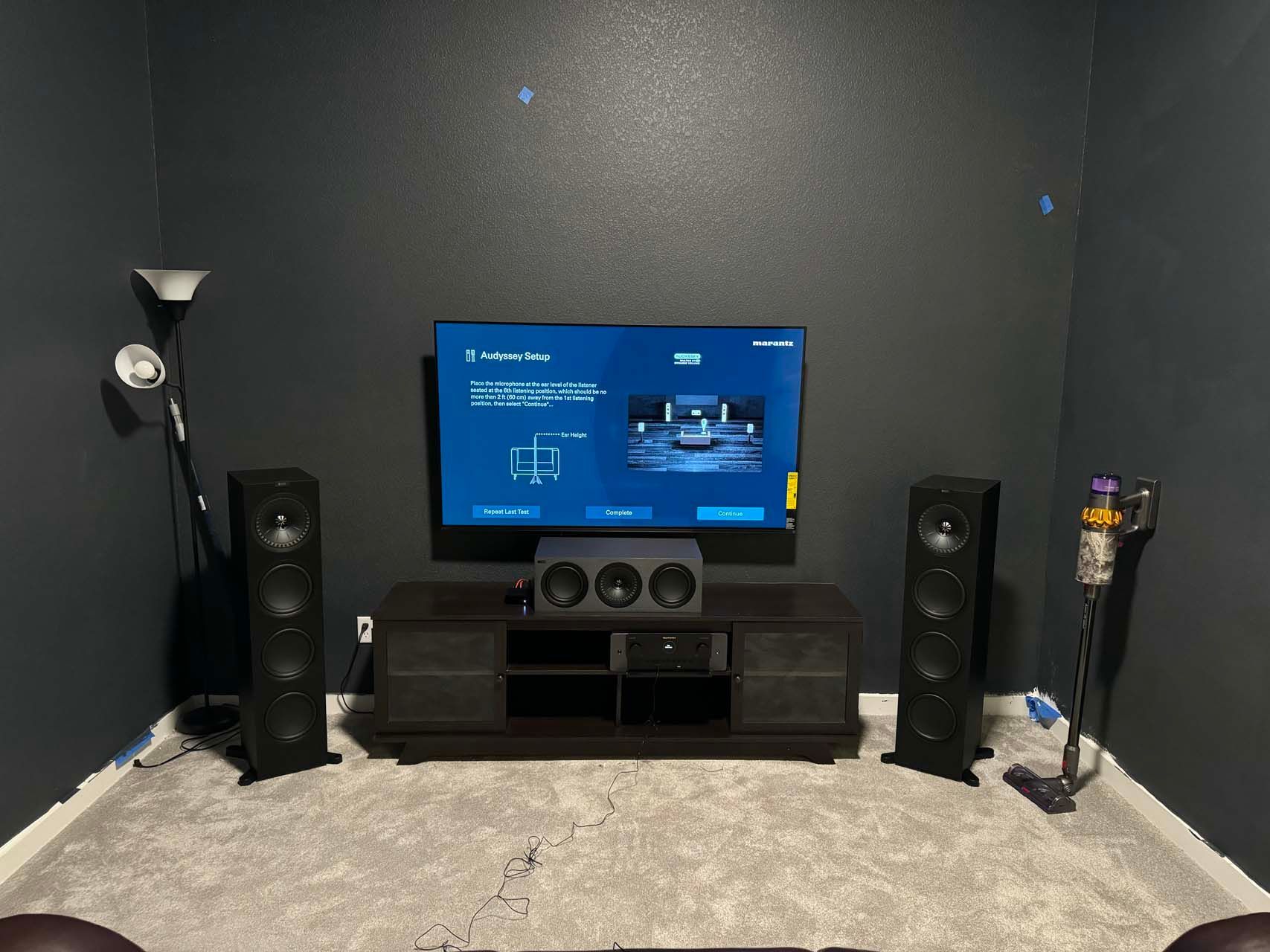 A living room with a television , speakers , and a vacuum cleaner.