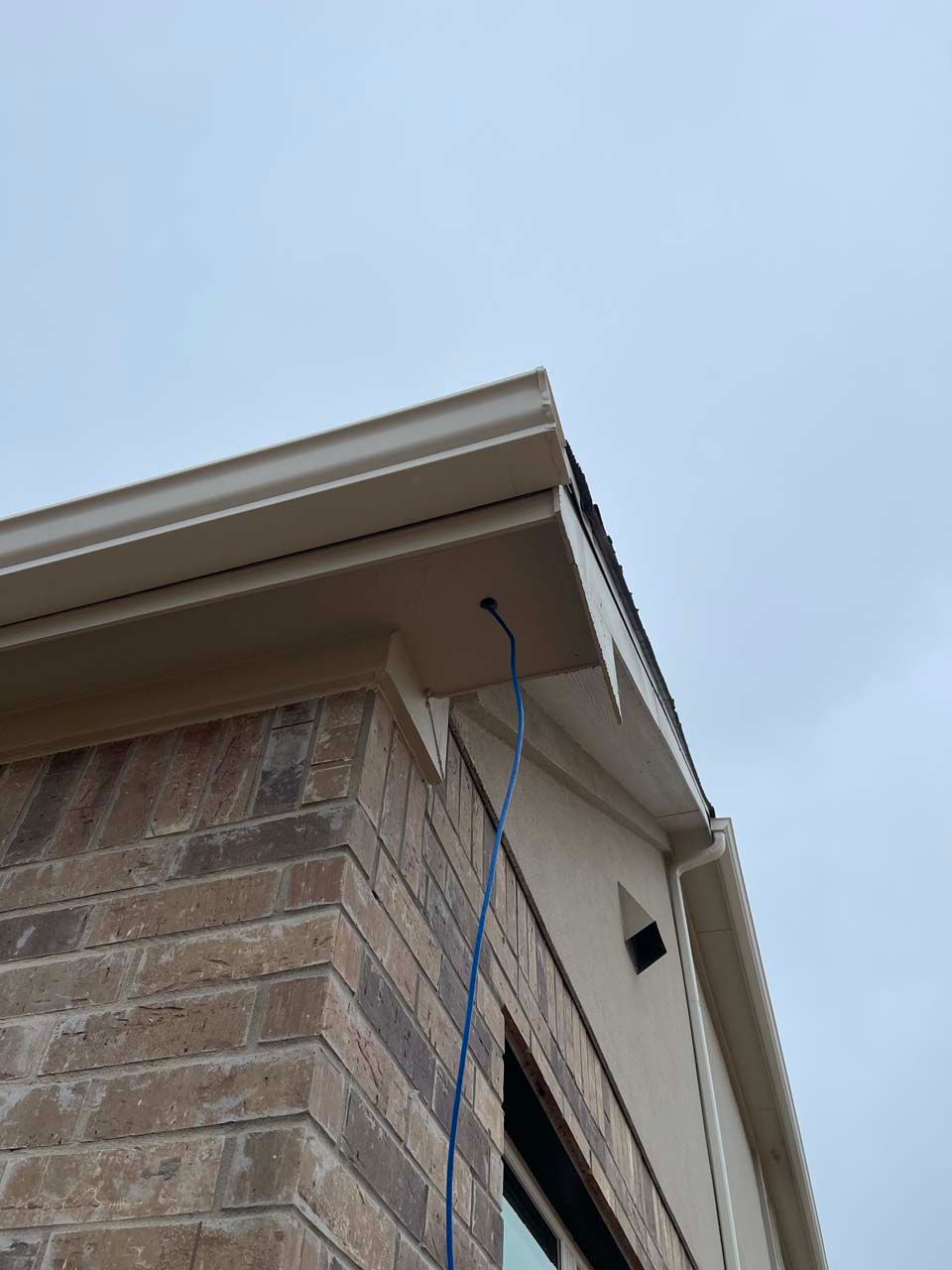A brick building with a white gutter and a blue hose attached to it.