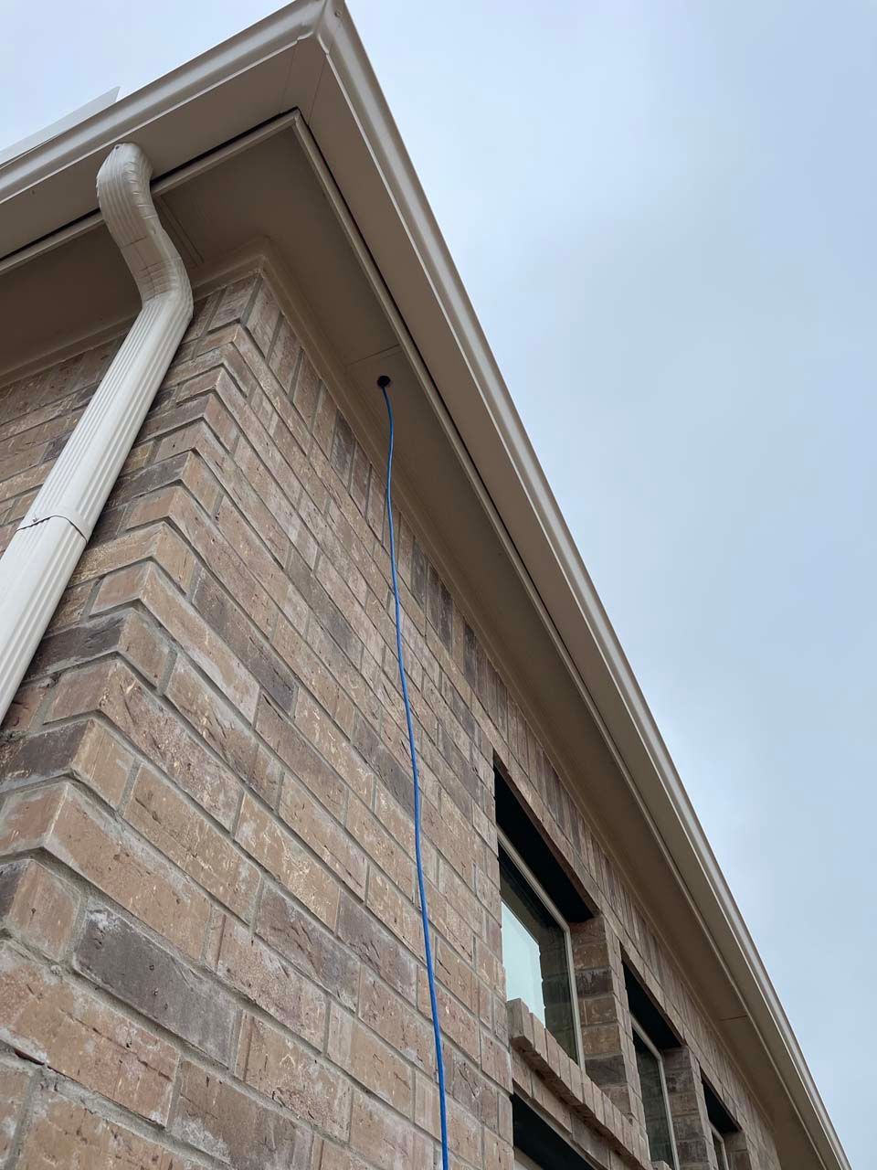 A brick building with a white gutter and a blue hose attached to it.