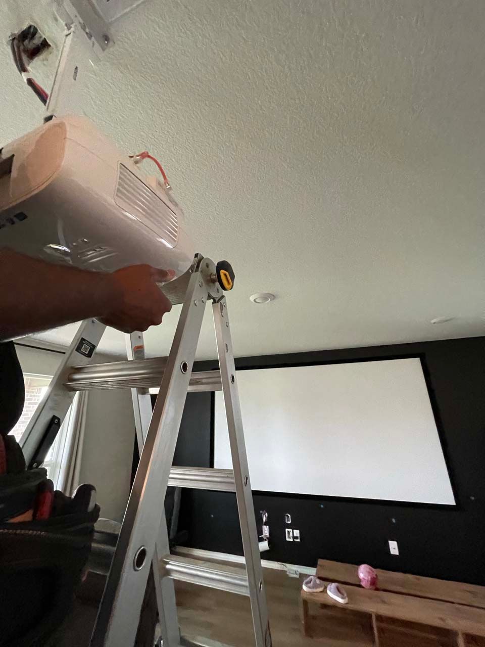 A man is standing on a ladder in a living room.