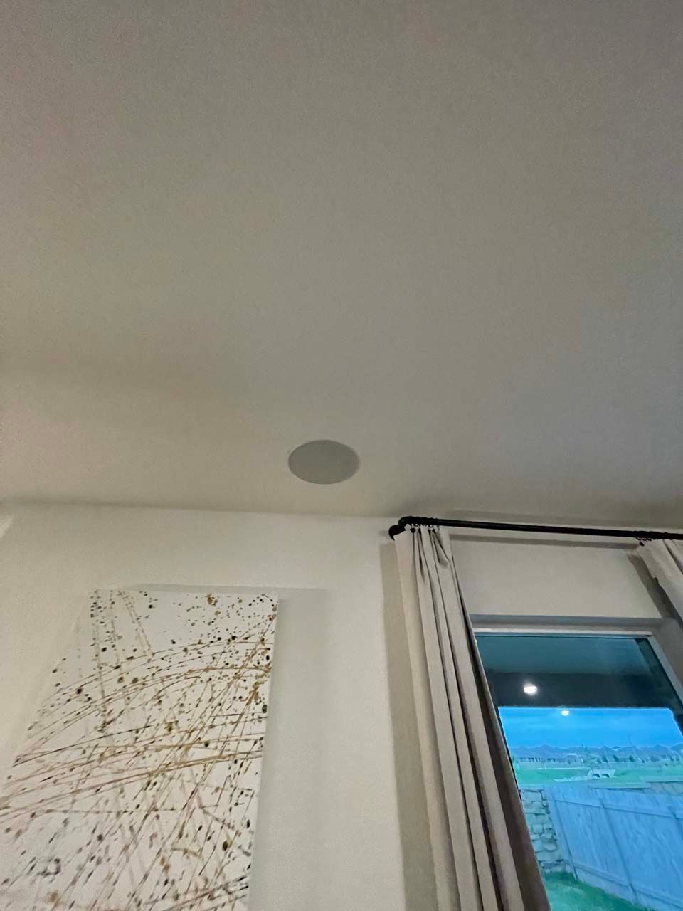 A living room with a ceiling speaker and a window.