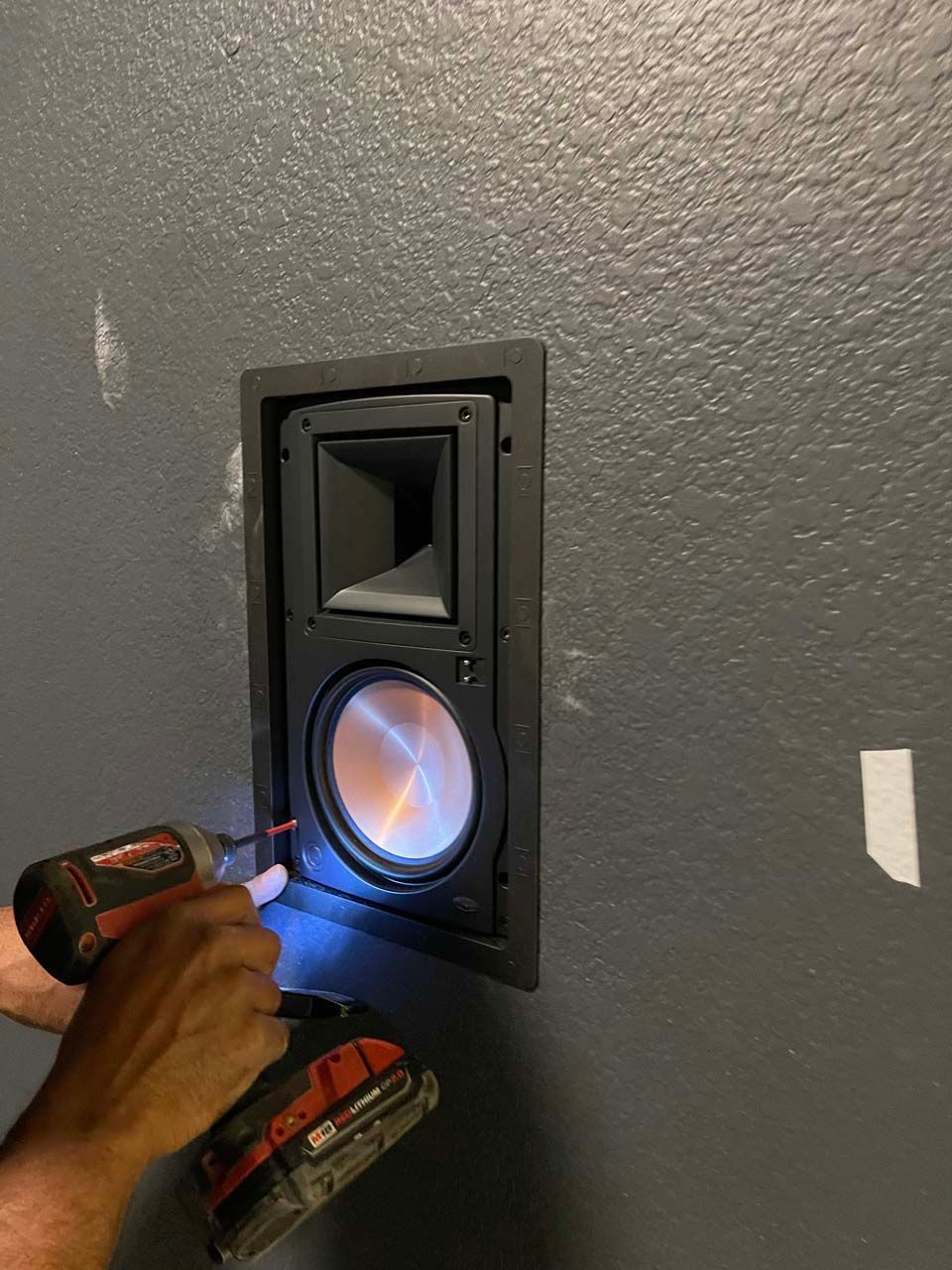 A person is installing a speaker in a wall with a drill.