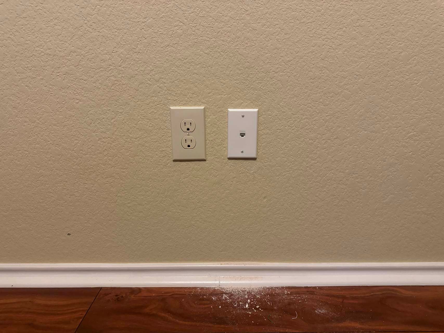 A room with two electrical outlets on the wall and a wooden floor.