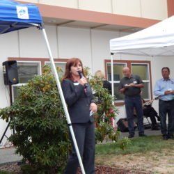 A woman speaking into a microphone under a blue tent
