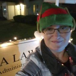 A woman is wearing a green elf hat and glasses.