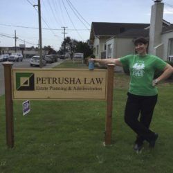 A woman in a green shirt is standing in front of a petrusha law sign.