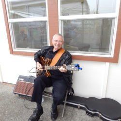 A man is sitting in front of a window playing a guitar.