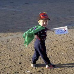 A young boy wearing a cape and a hat holds a flag with the number 23 on it