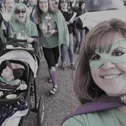 A woman wearing a green mask is taking a selfie with a group of people.