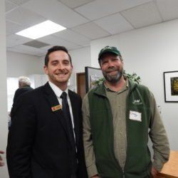 Two men are posing for a picture in a room . one of the men is wearing a green vest.