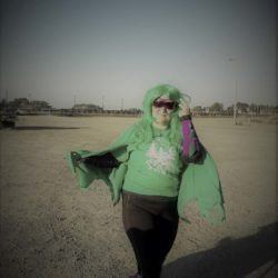 A woman wearing a green cape and sunglasses is standing in a field.