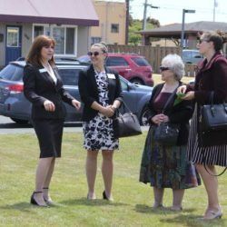 A group of women are standing in a grassy field talking to each other.
