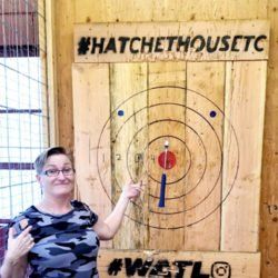 A woman is pointing at a target on a wooden wall.