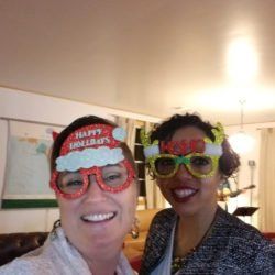 Two women wearing christmas glasses and hats are posing for a picture.