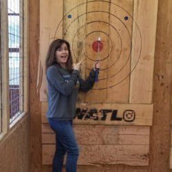 A woman is standing in front of a wooden target.