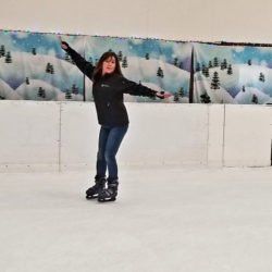 A woman is standing on an ice rink with her arms outstretched.