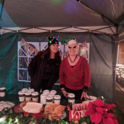 Two women are standing next to each other in front of a table with coffee cups.