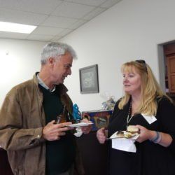 A man and a woman are standing next to each other holding plates of food.