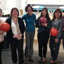 A group of women are standing in a bowling alley holding bowling balls.