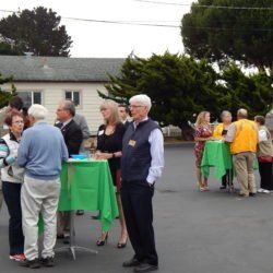 A group of people standing around green tables in a parking lot