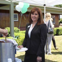 A woman in a black suit is standing under a tent with balloons in the background