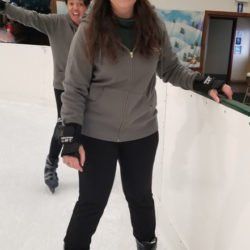 Two women are ice skating on an indoor rink.
