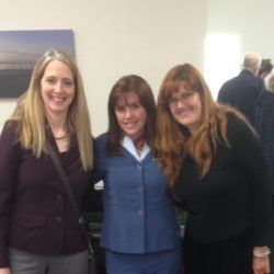 Three women posing for a picture with one wearing a blue suit