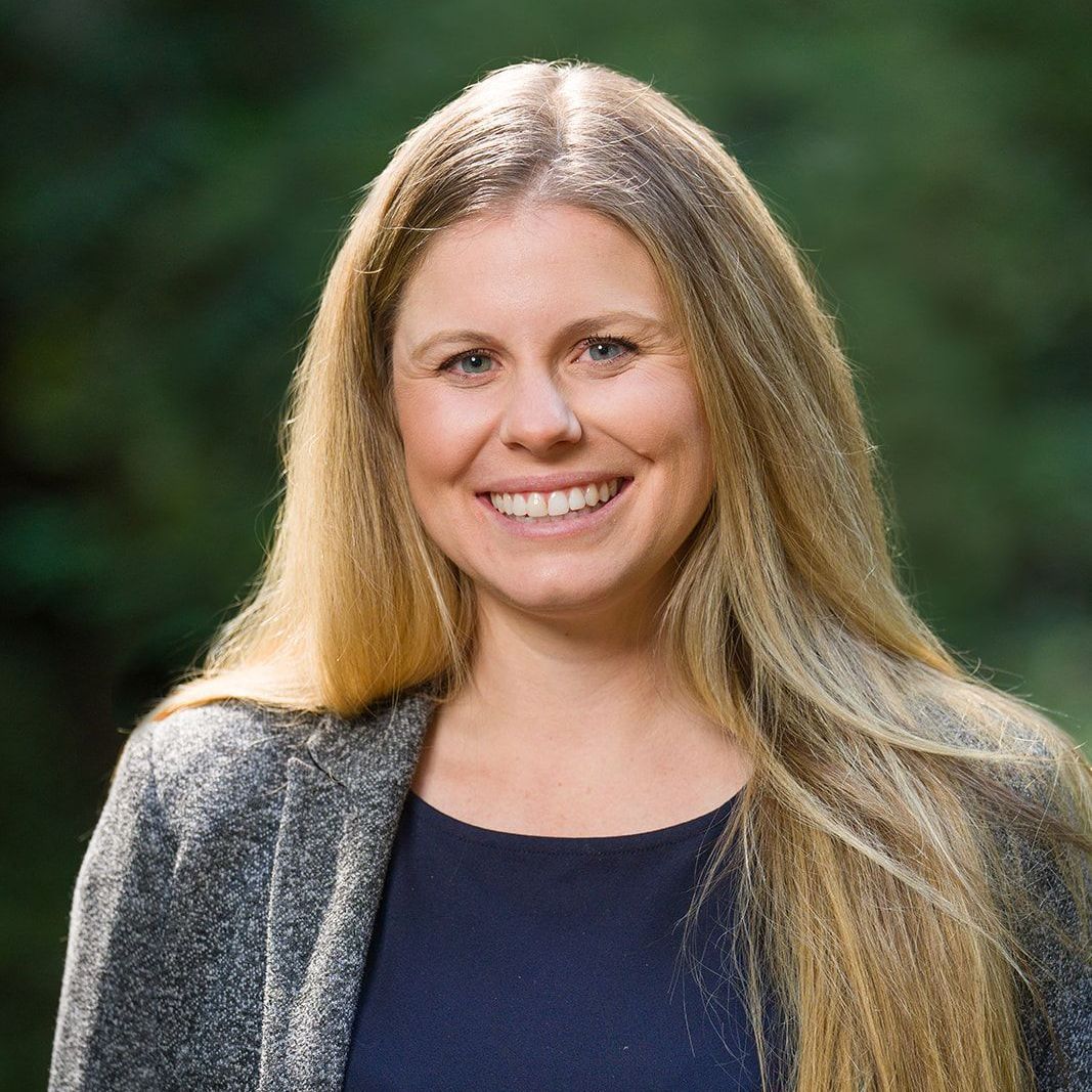 A woman wearing a plaid jacket and a black shirt is smiling for the camera.