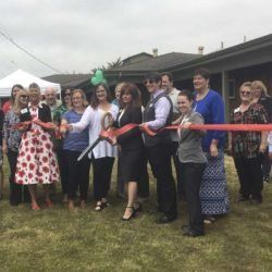 A group of people are standing in a field cutting a red ribbon.
