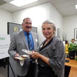 A man and a woman are standing next to each other in an office holding plates of food.