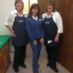 Three women wearing aprons are standing next to each other in a room.