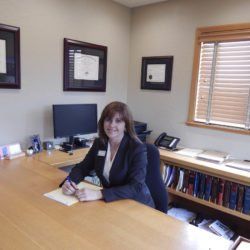 A woman in a suit sits at a desk in an office