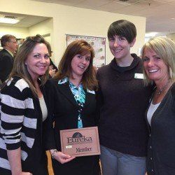 A group of women are posing for a picture while holding a sign that says eureka member.