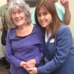 A woman in a blue jacket is hugging an older woman in a purple shirt.