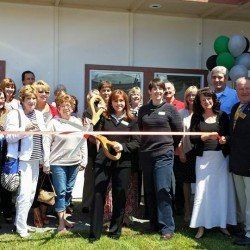 A group of people are standing in front of a building holding a ribbon.