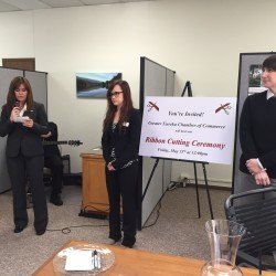 A group of people are standing in front of a sign that says ribbon cutting ceremony.