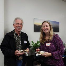 A man and a woman are standing next to each other holding plates of food.