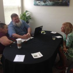 A group of people are sitting around a table with a laptop.